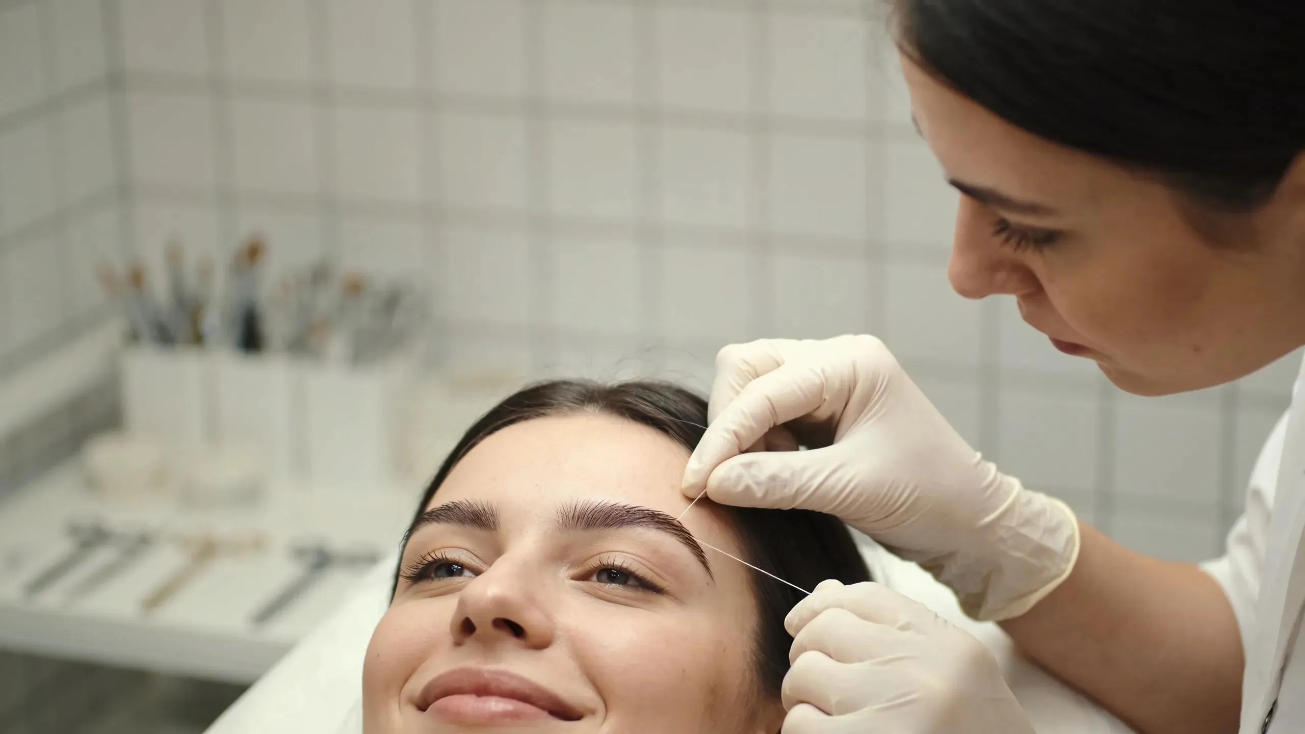 Aesthetician shaping eyebrows using threading techniques during a beauty treatment