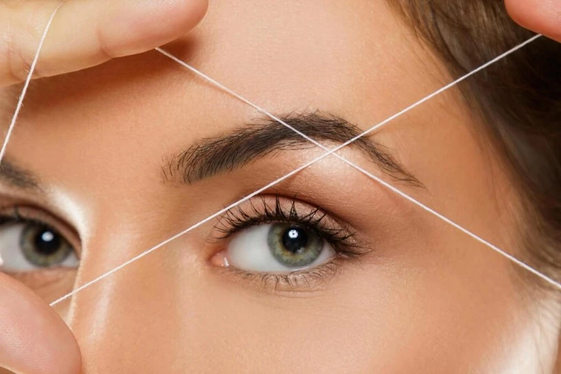 Certified esthetician performing precise eyebrow threading shaping technique