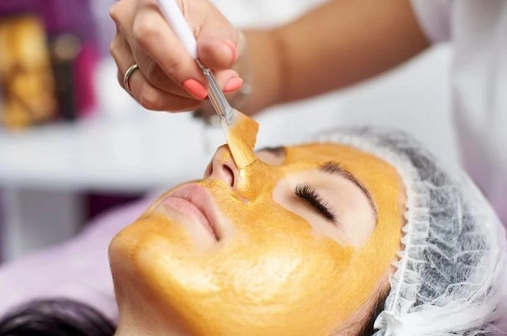 Esthetician applying a hydrating gold facial mask to skin